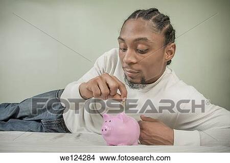 Young black man putting a United States quarter into a piggy bank. View Large Photo Image Picture - Young black man putting a United States quarter into a piggy bank.. Fotosearch