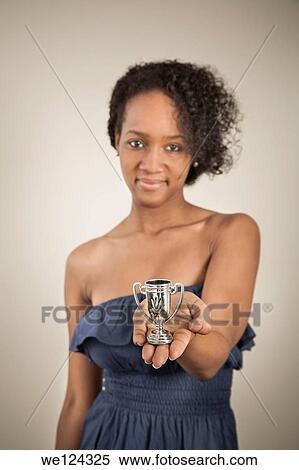 Stock Photography - Young black woman holding a very small trophy cup.. Fotosearch
