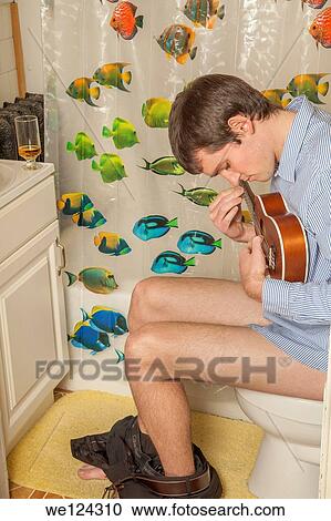 Young man sitting on the toilet playing a ukelele. View Large Photo Image Stock Image - Young man sitting on the toilet playing a ukelele.. Fotosearch