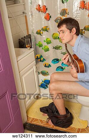 Young man sitting on the toilet playing a ukelele. View Large Photo Image Stock Image - Young man sitting on the toilet playing a ukelele.. Fotosearch