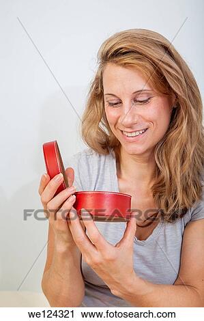 Stock Image - Young woman looking inside a round red container.. Fotosearch