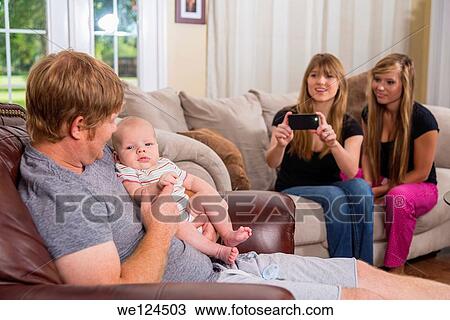 Father with baby boy and two young women in background taking picture with smart phone camera. View Large Photo Image Stock Image - Father with baby boy and two young women in background taking picture with smart phone camera.. Fotosearch