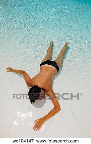 Stock Photo - A woman sunbathing on a white beach and crystal clear waters. Fotosearch