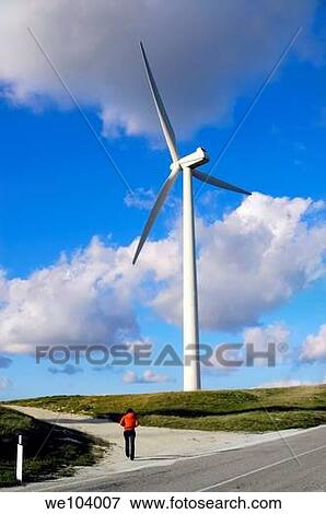Stock Photo - A woman walking towards a wind turbine. Fotosearch