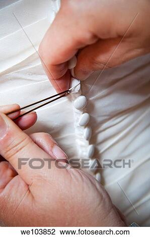 Stock Image - Hands buttoning up the bride's wedding dress. Fotosearch