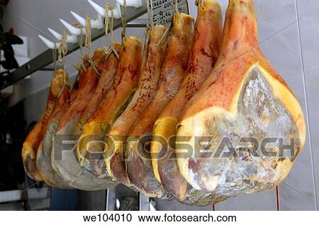 Stock Image - Prosciutto ham hanging from above in an Italian grocery stone Agnone Molise Italy. Fotosearch