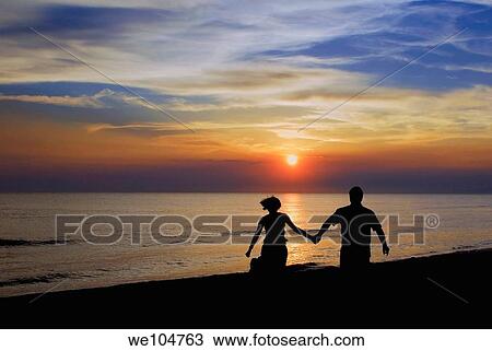 Stock Image - Romantic couple walking holding hands at sunset. Fotosearch