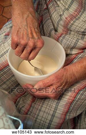 Stock Image - An old woman stirring homemade icing in a bowl on her lap. Fotosearch