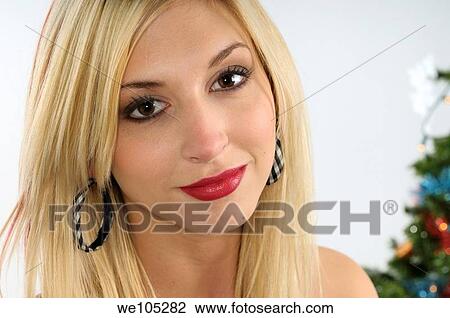 Stock Image - Close up of a smiling young blond woman standing by a Christmas tree. Fotosearch