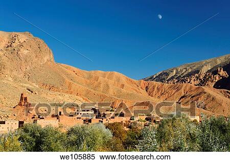 Stock Photography - Moon in blue sky over red soil and rock formations in Dades Gorge Morocco. Fotosearch