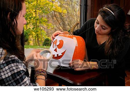 Two girls applying a stencil of a face onto a pumpkin for carving on Halloween View Large Photo Image Stock Image - Two girls applying a stencil of a face onto a pumpkin for carving on Halloween. Fotosearch