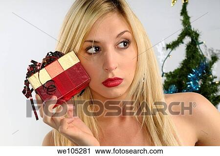 Young blond woman holding a Christmas present up to her cheek by a Christmas tree View Large Photo Image Stock Image - Young blond woman holding a Christmas present up to her cheek by a Christmas tree. Fotosearch
