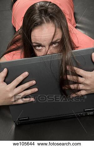 Young woman lying on a mat, looking over the top of her laptop computer View Large Photo Image Picture - Young woman lying on a mat, looking over the top of her laptop computer. Fotosearch