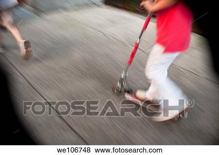 Stock Photo - A blurry photo of a child on a push scooter on a sidewalk in New York City.. Fotosearch