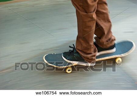 A leg view of a boy wearing brown pants and black sneaker riding a skateboard on a sidewalk. View Large Photo Image Picture - A leg view of a boy wearing brown pants and black sneaker riding a skateboard on a sidewalk.. Fotosearch