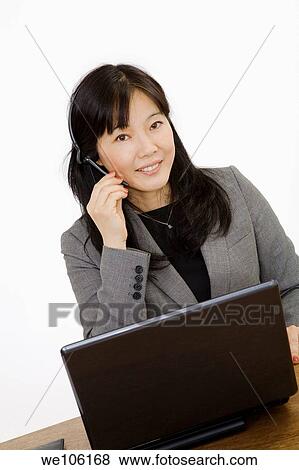 Beautiful Asain Businesswoman working on a laptop computer and talking on a telephone headset She is photographed on a white background View Large Photo Image Stock Photo - Beautiful Asain Businesswoman working on a laptop computer and talking on a telephone headset She is photographed on a white background. Fotosearch