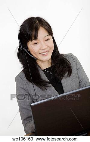 Beautiful Asain Businesswoman working on a laptop computer and talking on a telephone headset She is photographed on a white background View Large Photo Image Stock Photo - Beautiful Asain Businesswoman working on a laptop computer and talking on a telephone headset She is photographed on a white background. Fotosearch