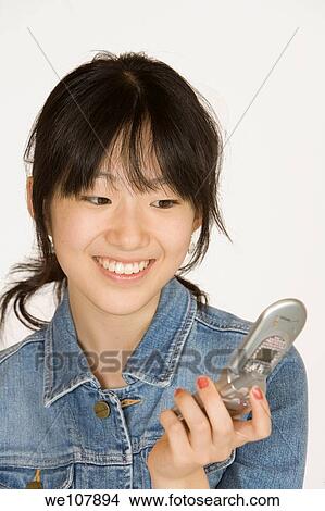 Portrait of a beautiful Asian teenager talking on a cell phone on a white background View Large Photo Image Picture - Portrait of a beautiful Asian teenager talking on a cell phone on a white background. Fotosearch