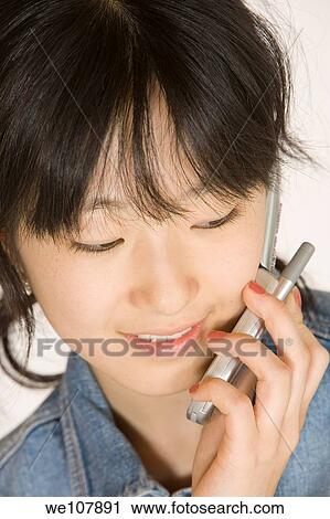 Stock Image - Portrait of a beautiful Asian teenager talking on a cell phone on a white background. Fotosearch