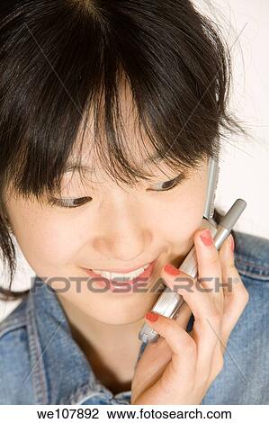 Stock Image - Portrait of a beautiful Asian teenager talking on a cell phone on a white background. Fotosearch