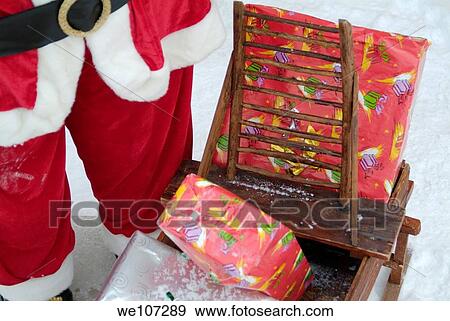 Stock Photo - Santa Claus toy standing next to Christmas presents in the snow. Fotosearch