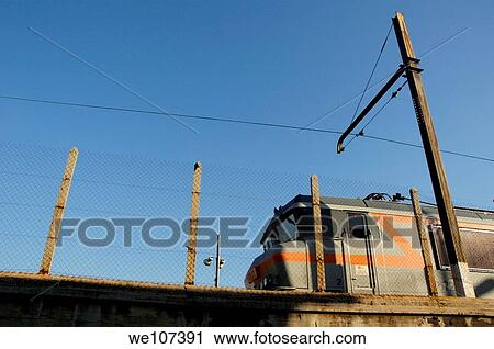Stock Image - Train travelling being a barbed wire fence against a blue sky, Marseille, France. Fotosearch