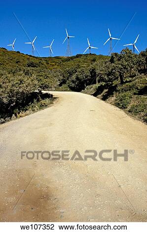 Stock Image - Wind turbines on hill above dirt road, Tarifa, Andalusia, Spain. Fotosearch