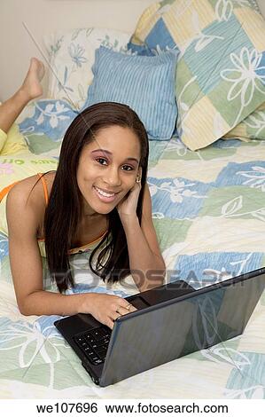 African American teen laying on the bed and working on laptop computer View Large Photo Image Stock Photograph - African American teen laying on the bed and working on laptop computer. Fotosearch