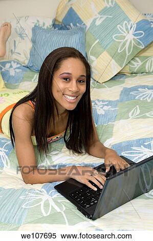 Stock Photography - African American teen working on laptop computer in her bedroom. Fotosearch