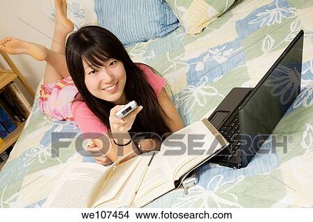 Asian American teen watching television while doing homework View Large Photo Image Picture - Asian American teen watching television while doing homework. Fotosearch