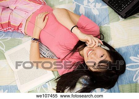 Stock Photography - Asian American teen working on homework and talking on cell phone. Fotosearch