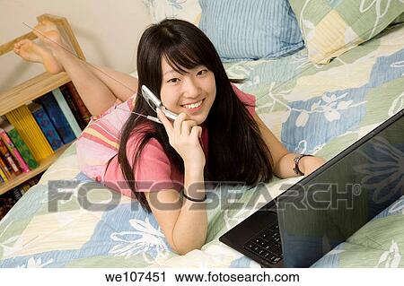Asian American teen working on laptop computer and talking on cell phone View Large Photo Image Stock Image - Asian American teen working on laptop computer and talking on cell phone. Fotosearch