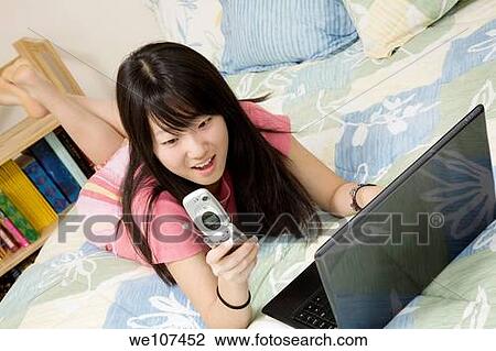 Asian American teen working on laptop computer and talking on cell phone View Large Photo Image Stock Image - Asian American teen working on laptop computer and talking on cell phone. Fotosearch