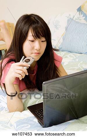 Asian American teen working on laptop computer and talking on cell phone View Large Photo Image Stock Image - Asian American teen working on laptop computer and talking on cell phone. Fotosearch