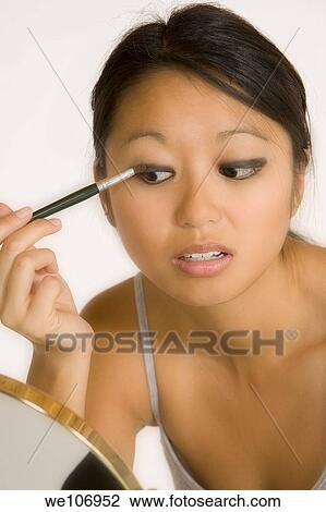 Stock Image - Asian woman applying eye shadow. Fotosearch