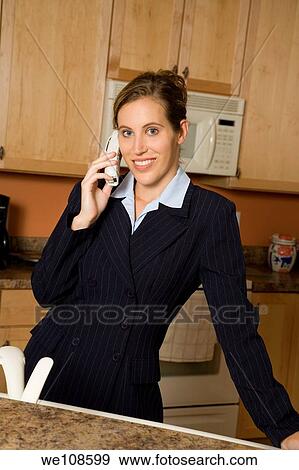 Businesswoman in early 20s standing in the kitchen dresses in a business suit and talking on the telephone View Large Photo Image Stock Photo - Businesswoman in early 20s standing in the kitchen dresses in a business suit and talking on the telephone. Fotosearch