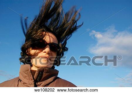 Stock Image - Portrait of a woman wearing sunglasses on a windy day. Fotosearch