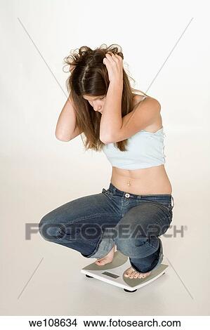 Teenage girl weighting herself and up set because her feels she is gaining weight View Large Photo Image Picture - Teenage girl weighting herself and up set because her feels she is gaining weight. Fotosearch