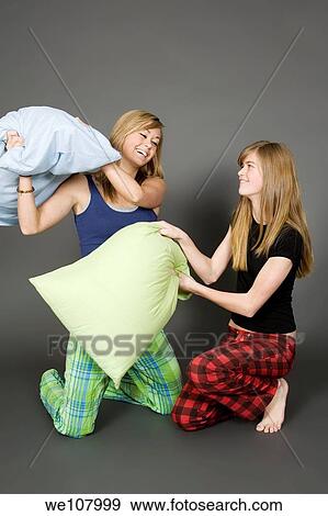 Teenage sisters having a pillow fight on a gray background View Large Photo Image Stock Photo - Teenage sisters having a pillow fight on a gray background. Fotosearch