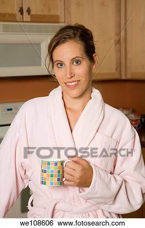 Woman in early 20s standing in the kitchen dressed in a robe and holding a coffee cup View Large Photo Image Stock Photograph - Woman in early 20s standing in the kitchen dressed in a robe and holding a coffee cup. Fotosearch
