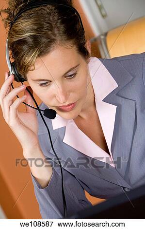 Woman in early 20s working on computer and talking on headset telephone at home View Large Photo Image Stock Photo - Woman in early 20s working on computer and talking on headset telephone at home. Fotosearch