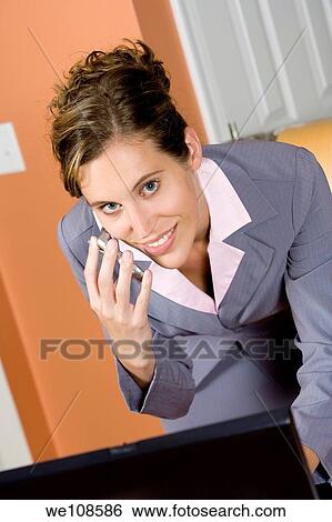 Stock Photograph - Woman in early 20s working on computer and talking on headset telephone at home. Fotosearch