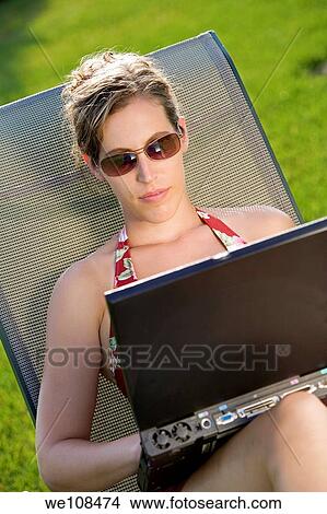 Woman in mid 20s sunbathing and working on a laptop computer View Large Photo Image Picture - Woman in mid 20s sunbathing and working on a laptop computer. Fotosearch