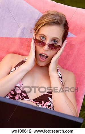 Stock Image - Woman in mid 20s working on a laptop with a surprised look. Fotosearch