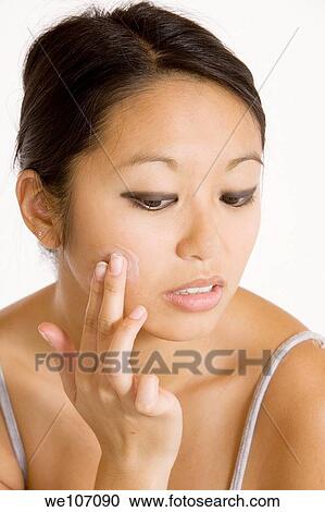 Stock Image - Young Asian woman applying moisturizing cream on her face. Fotosearch