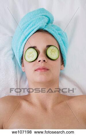 Stock Photo - Young woman having a relaxing moment during a message with cucumbers laying on her eyes. Fotosearch