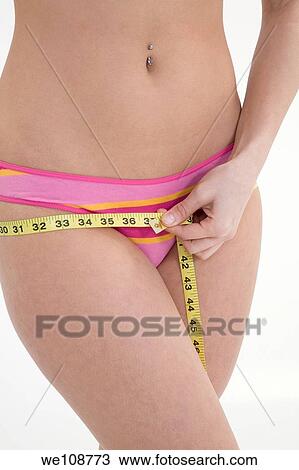 Stock Image - Young woman in underwear measuring her hips. Fotosearch