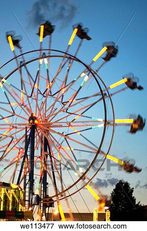 Stock Photo - A Ferris Wheel in motion as the sun sets on a County Fair. Fotosearch