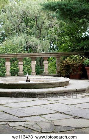 Stock Image - A low fountain next to some potted plants and stone railing. Fotosearch