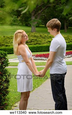 Stock Image - Couple in love holding hands looking at each other in a park. Fotosearch